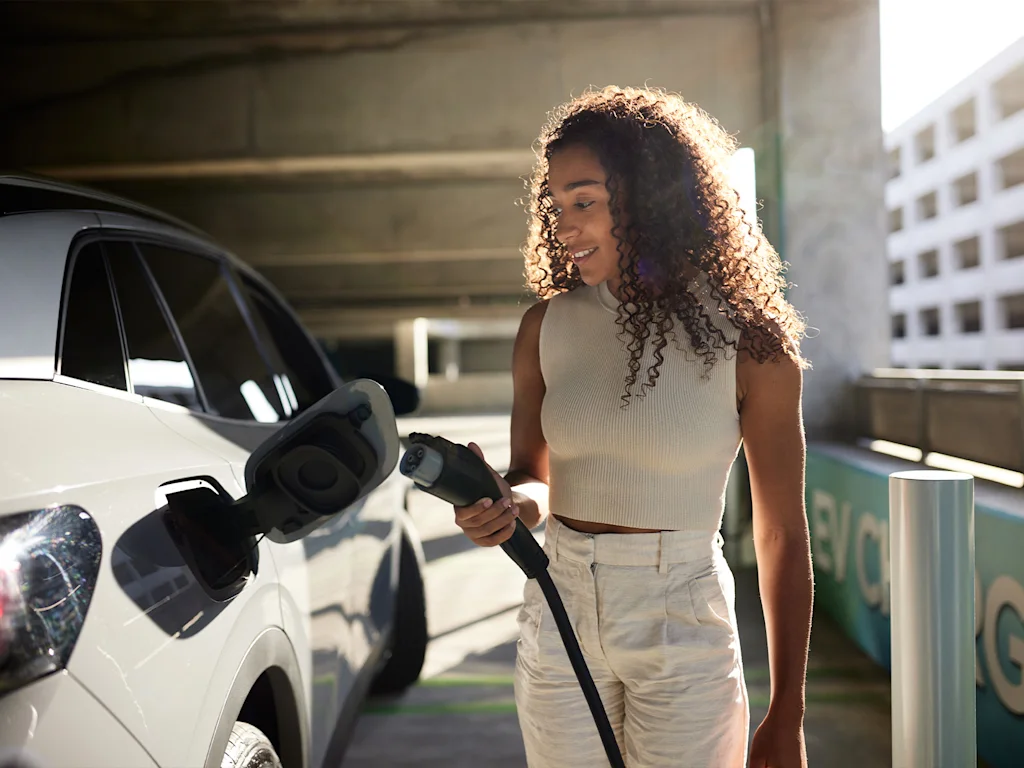 A woman charging her electric vehicle at a charging station.