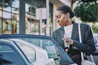 Woman holding phone opening car door