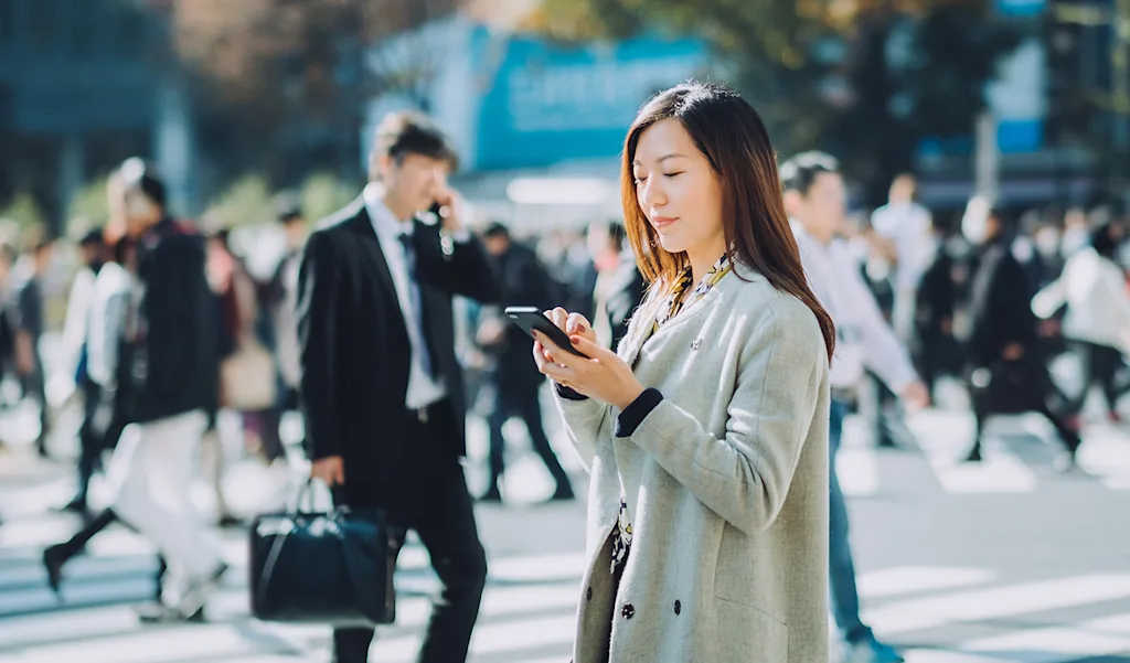 街なかでスマートフォンを使いながら正確なジオコーディングで高精度位置情報を取得する女性