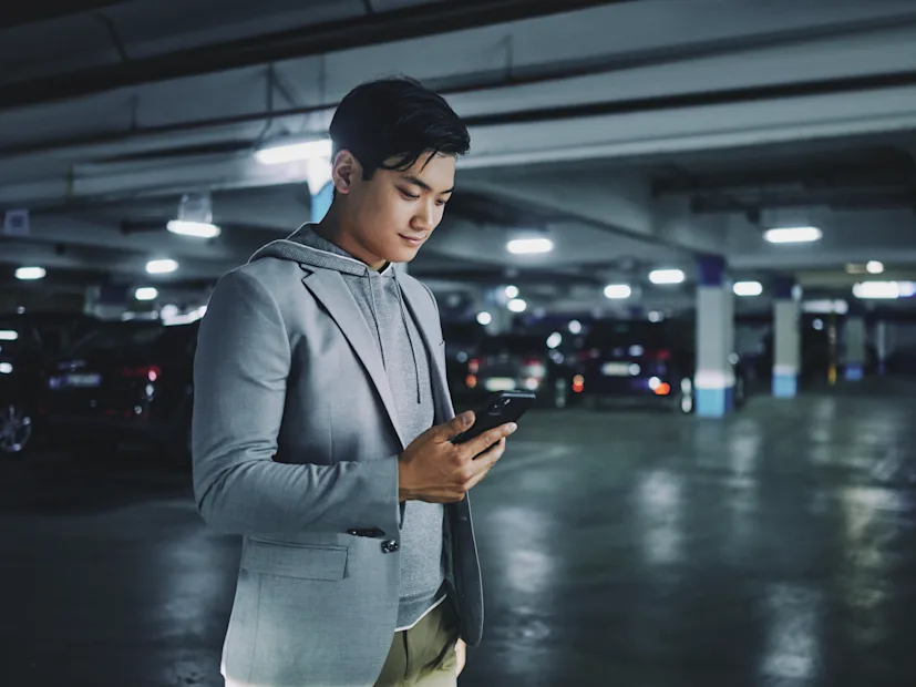 A man looks at his smartphone in a parking garage.