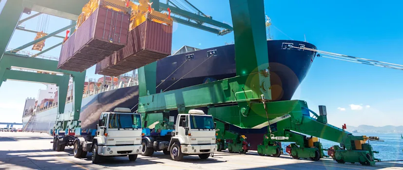 Two trucks prepare to be loaded with shipping containers at a port.